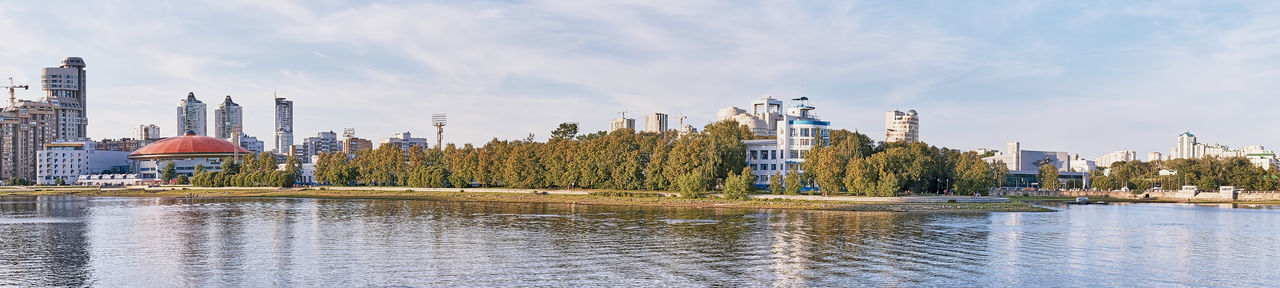 Panoramic view of buildings by river against sky.