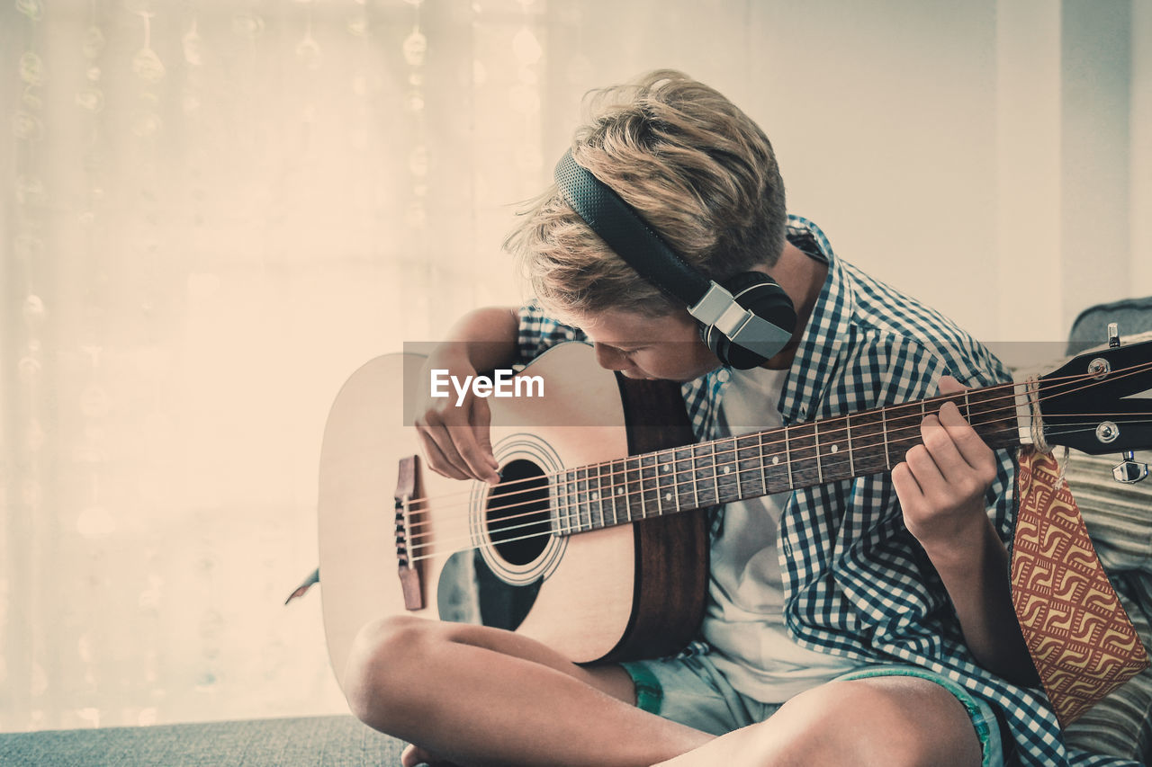 Boy playing guitar while sitting at home