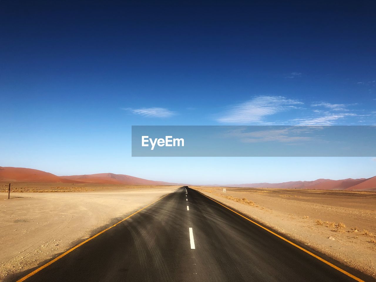 Diminishing perspective of road passing through desert against sky during sunny day