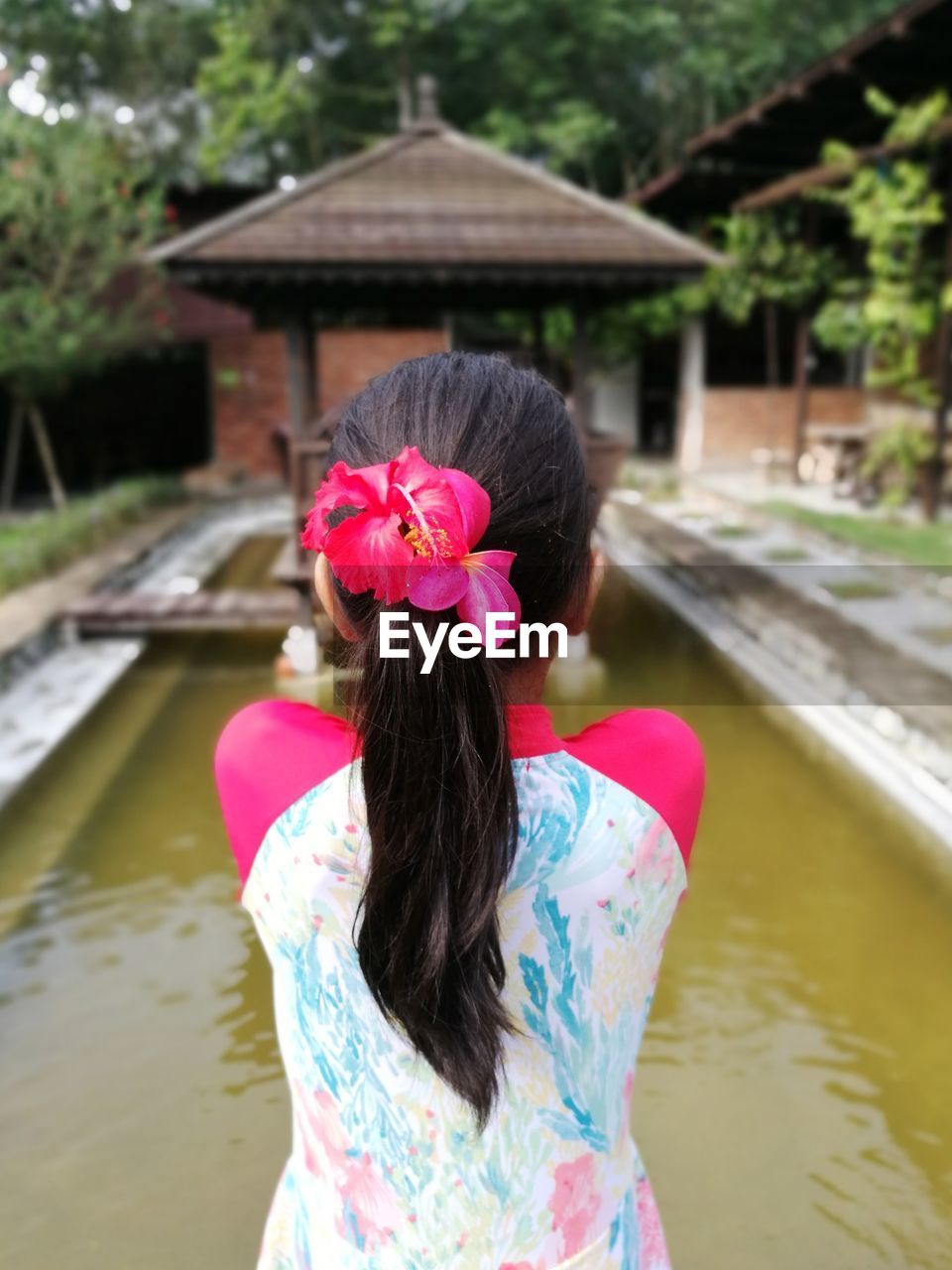 Rear view of woman standing by pond against built structure