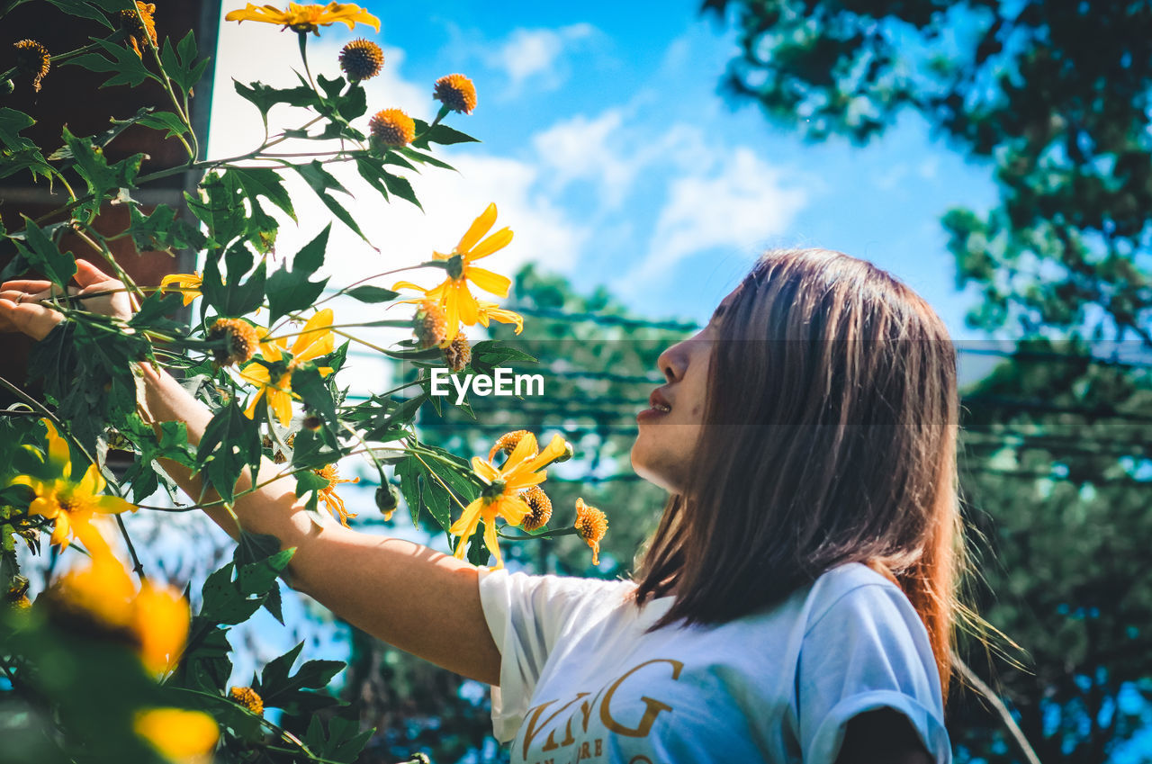 Close-up of woman looking at flowering plants against sky