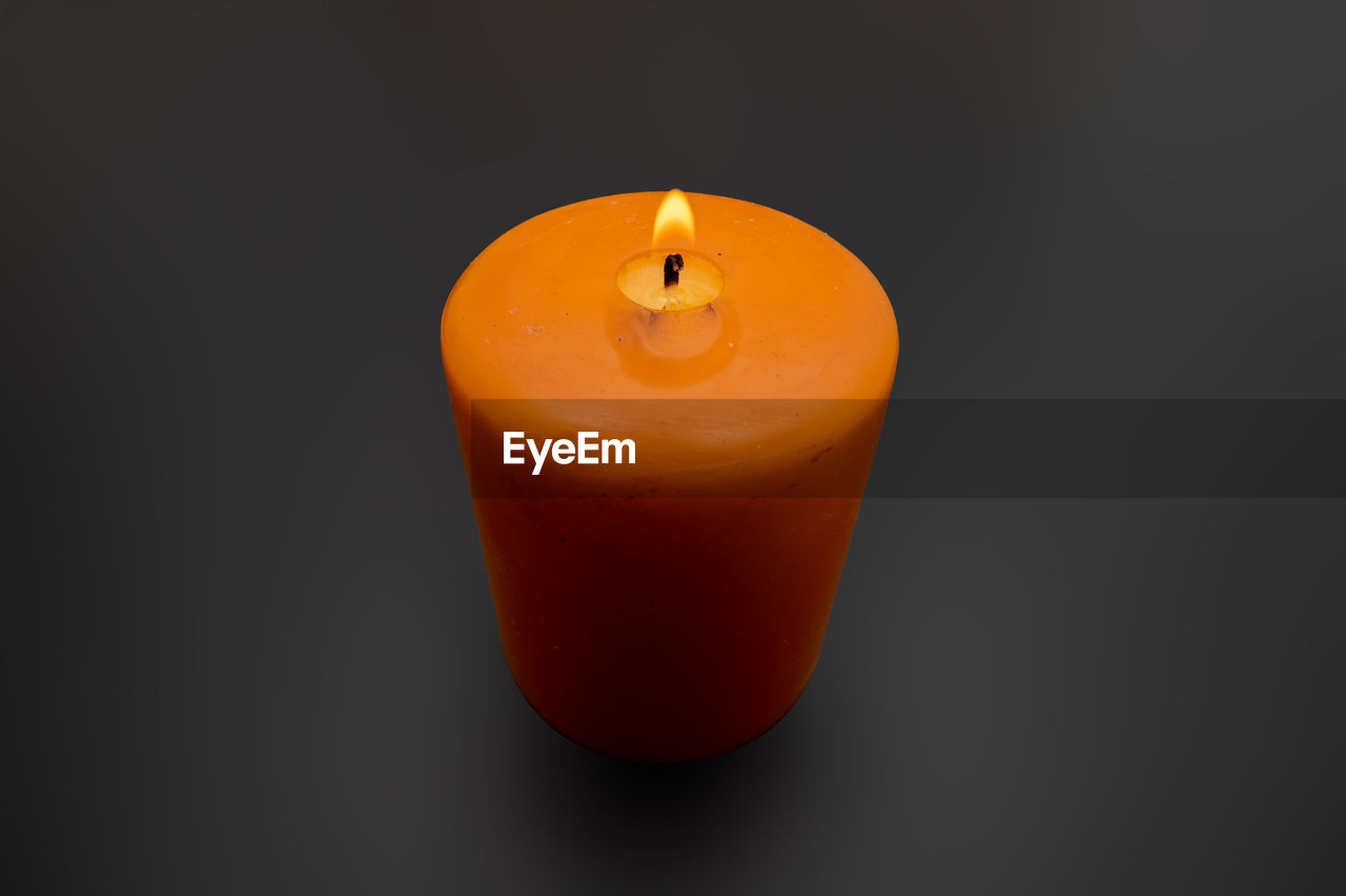 CLOSE-UP OF LIT CANDLE AGAINST ORANGE BACKGROUND