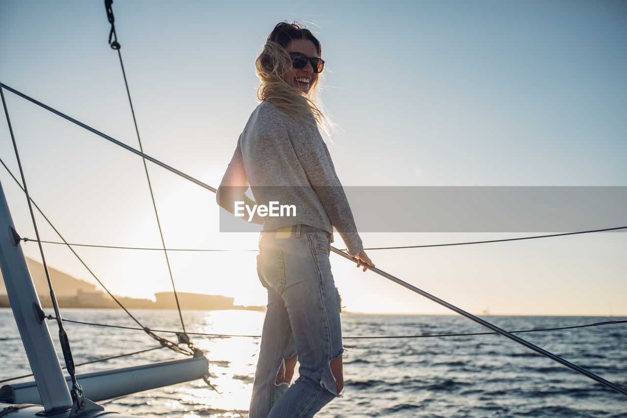 LOW ANGLE VIEW OF YOUNG WOMAN FISHING IN SEA AGAINST SKY