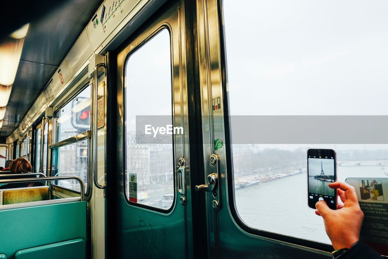 Cropped hand photographing eiffel tower through mobile phone while traveling in train