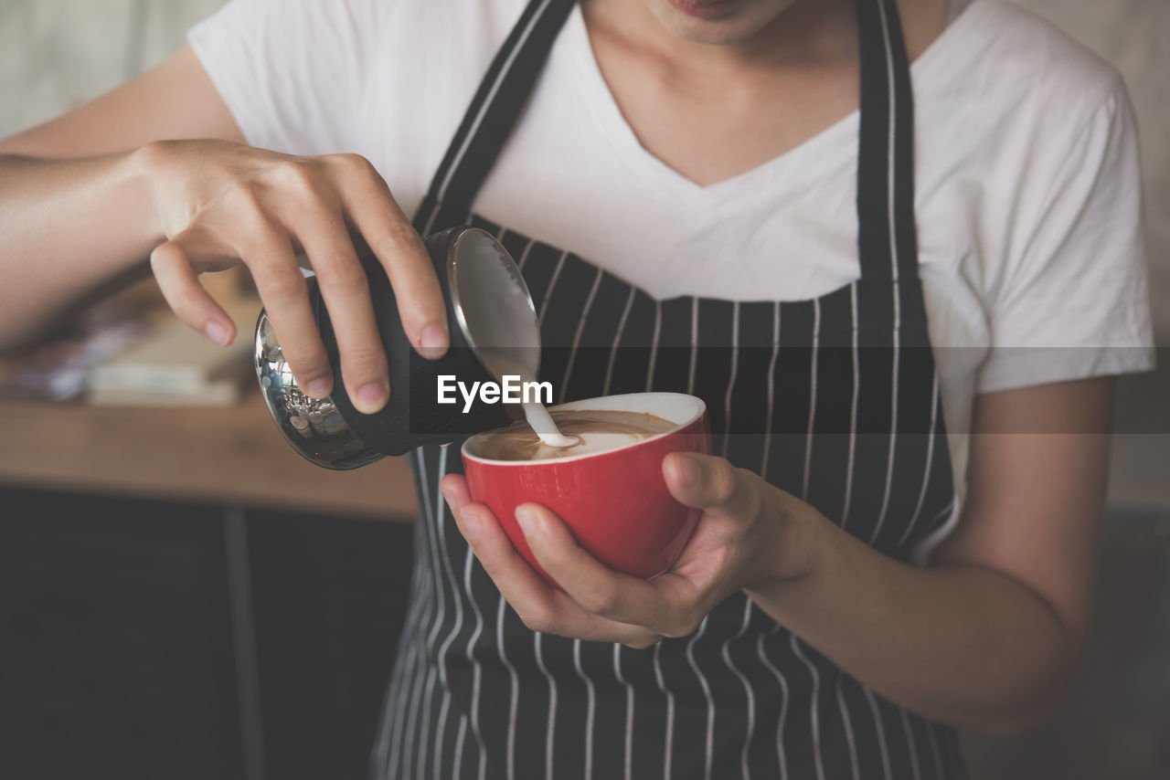 Midsection of woman pouring milk in coffee cup