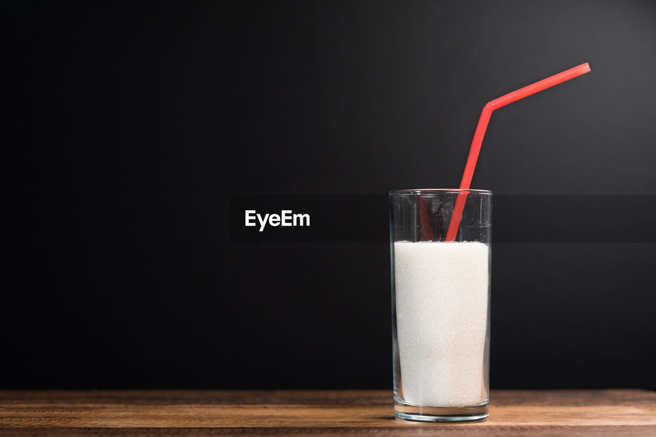 A glass of white sugar with straw against black background. concept of unhealthy eating and diabetis