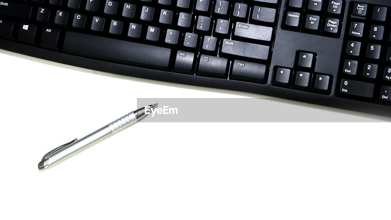 High angle view of computer keyboard and pen over white background