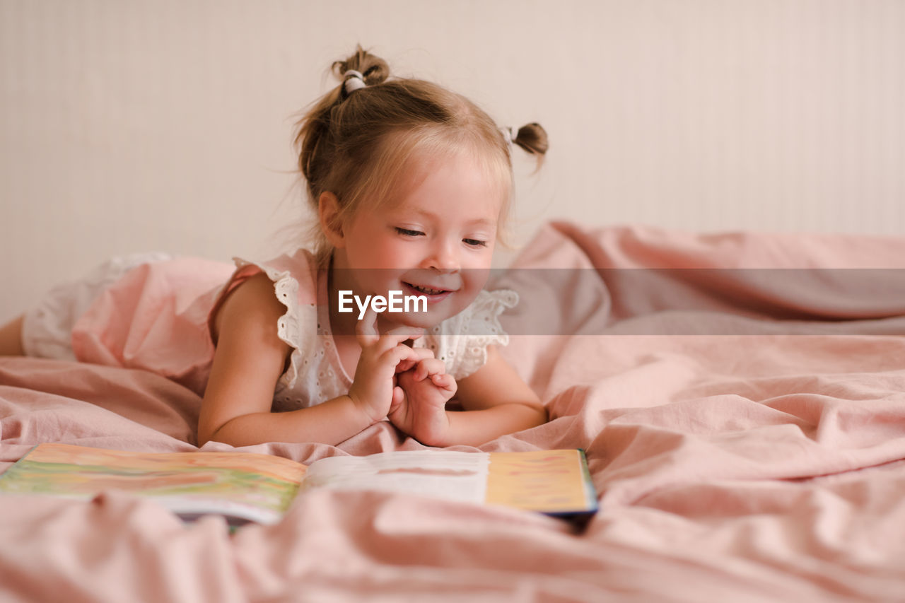 Pretty little child girl 2-3 year old reading book lying in bed closeup. good morning. childhood.