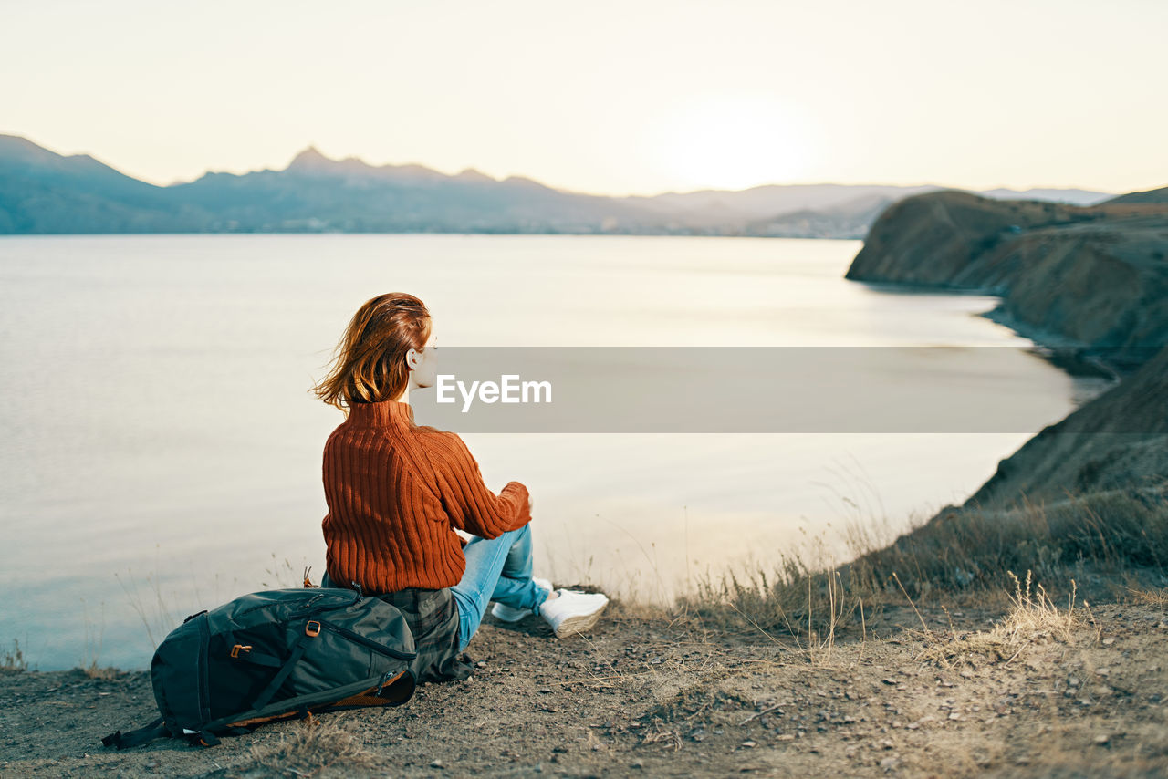 WOMAN SITTING ON LAND AGAINST THE SKY