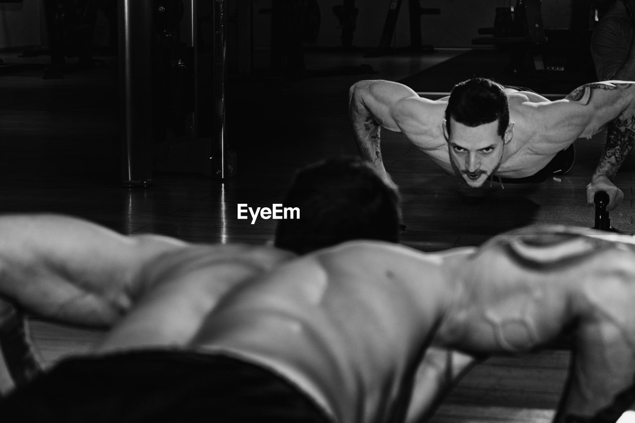 Rear view of shirtless man exercising against mirror at gym