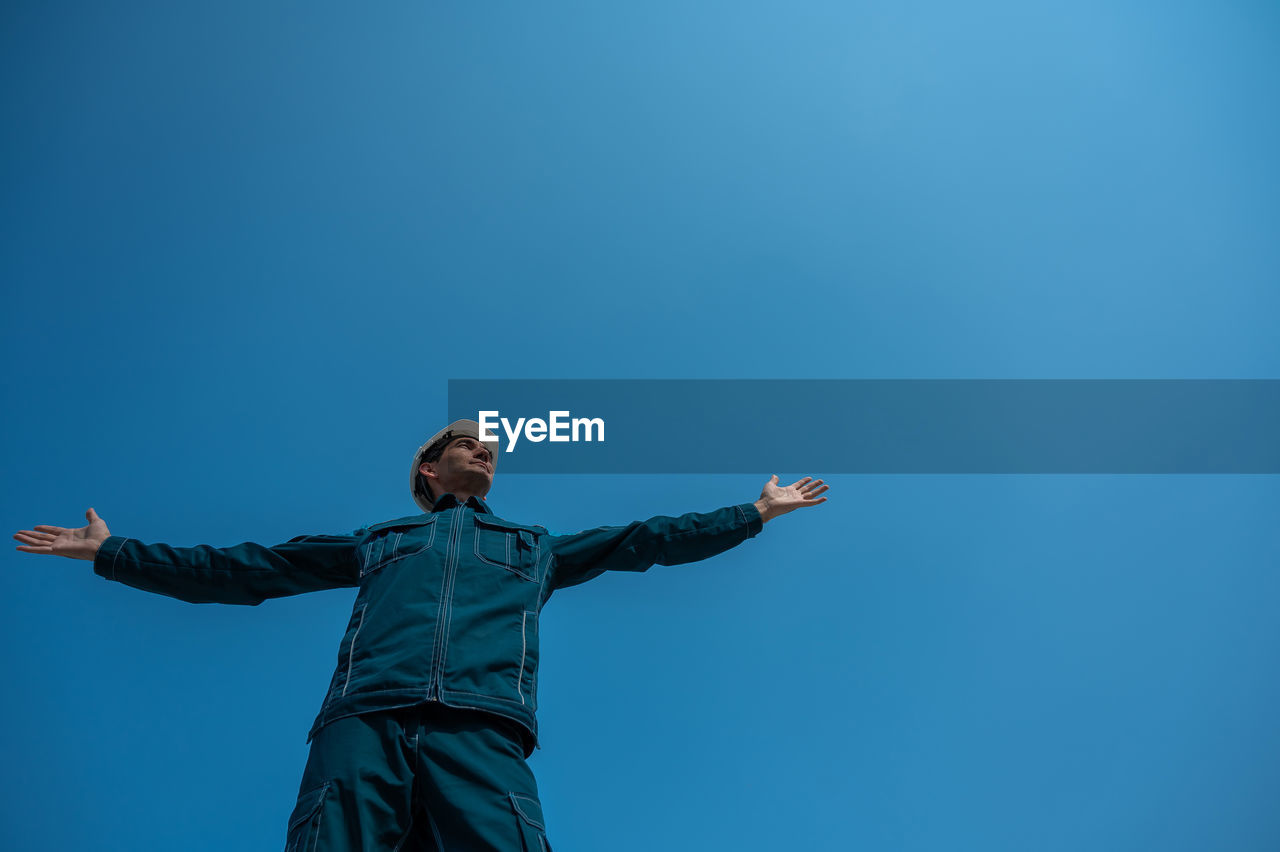 low angle view of woman with arms raised standing against clear sky