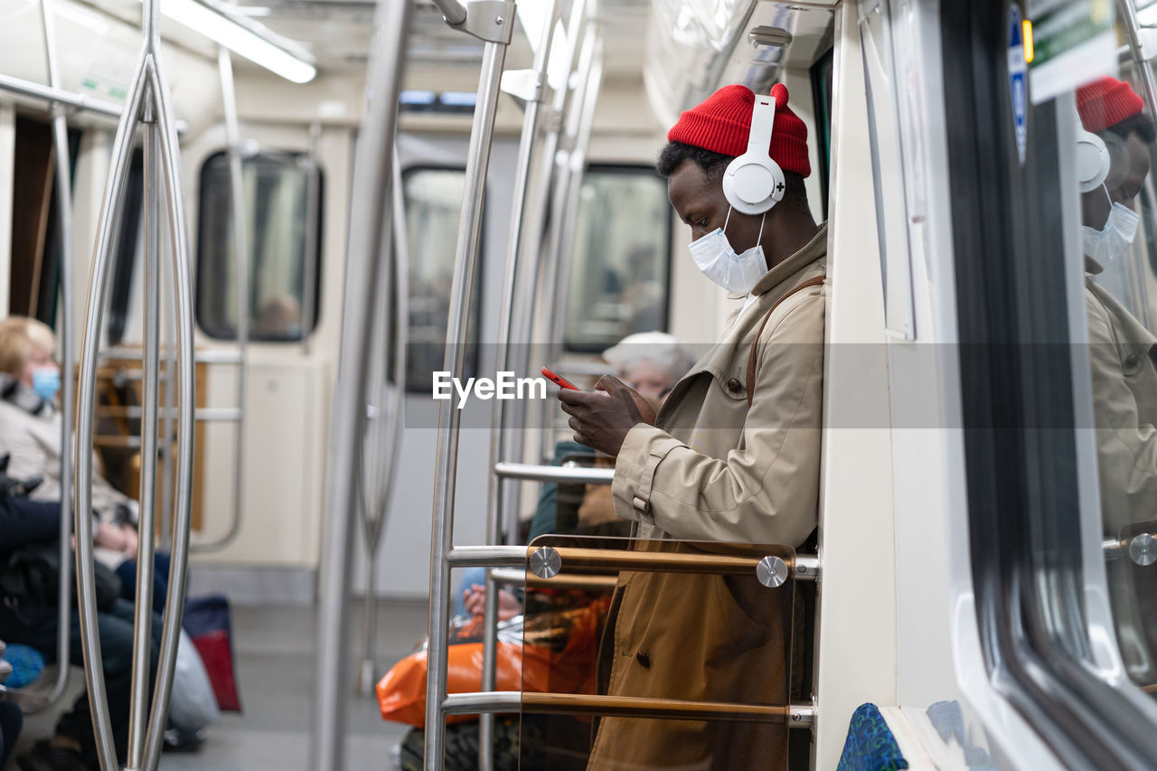 Side view of man wearing mask using mobile phone in train