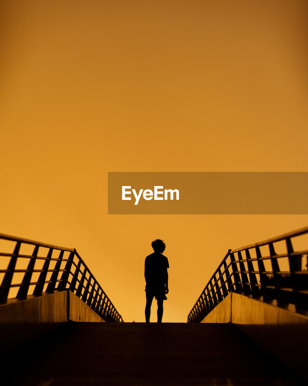 SILHOUETTE MAN WALKING ON STAIRCASE AGAINST ORANGE SKY