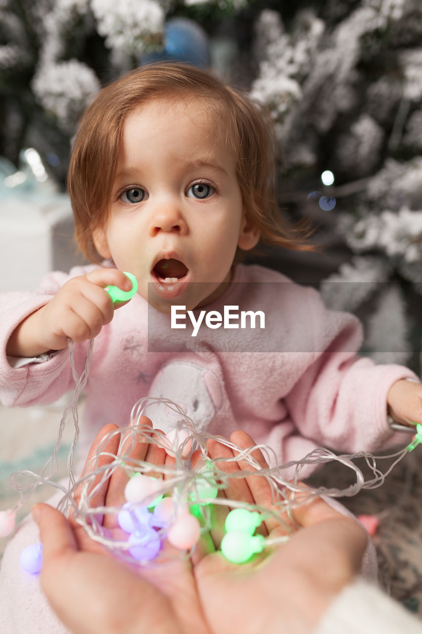 Portrait of cute girl holding christmas lights while sitting at home