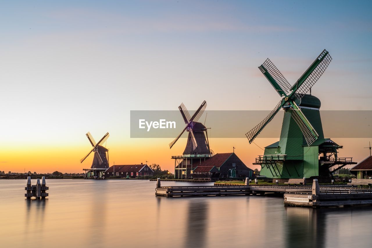 Traditional windmill by river against sky during sunset