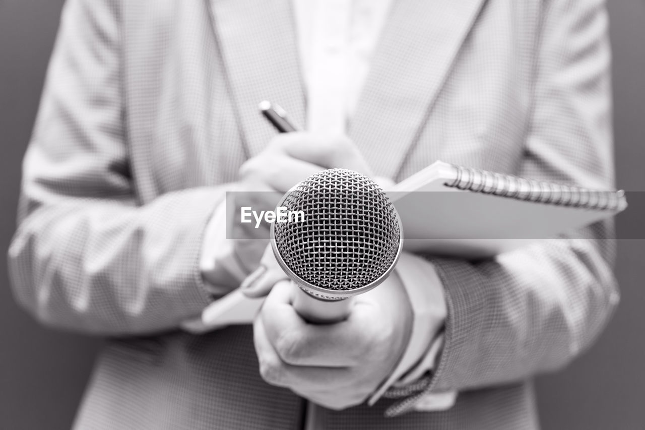 Reporter or tv journalist at press conference or media event, holding microphone and writing notes