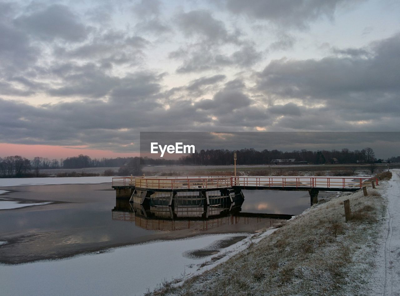 Pier on frozen river against cloudy sky