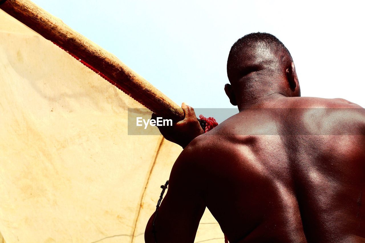 Low angle view of shirtless man holding wood against sky