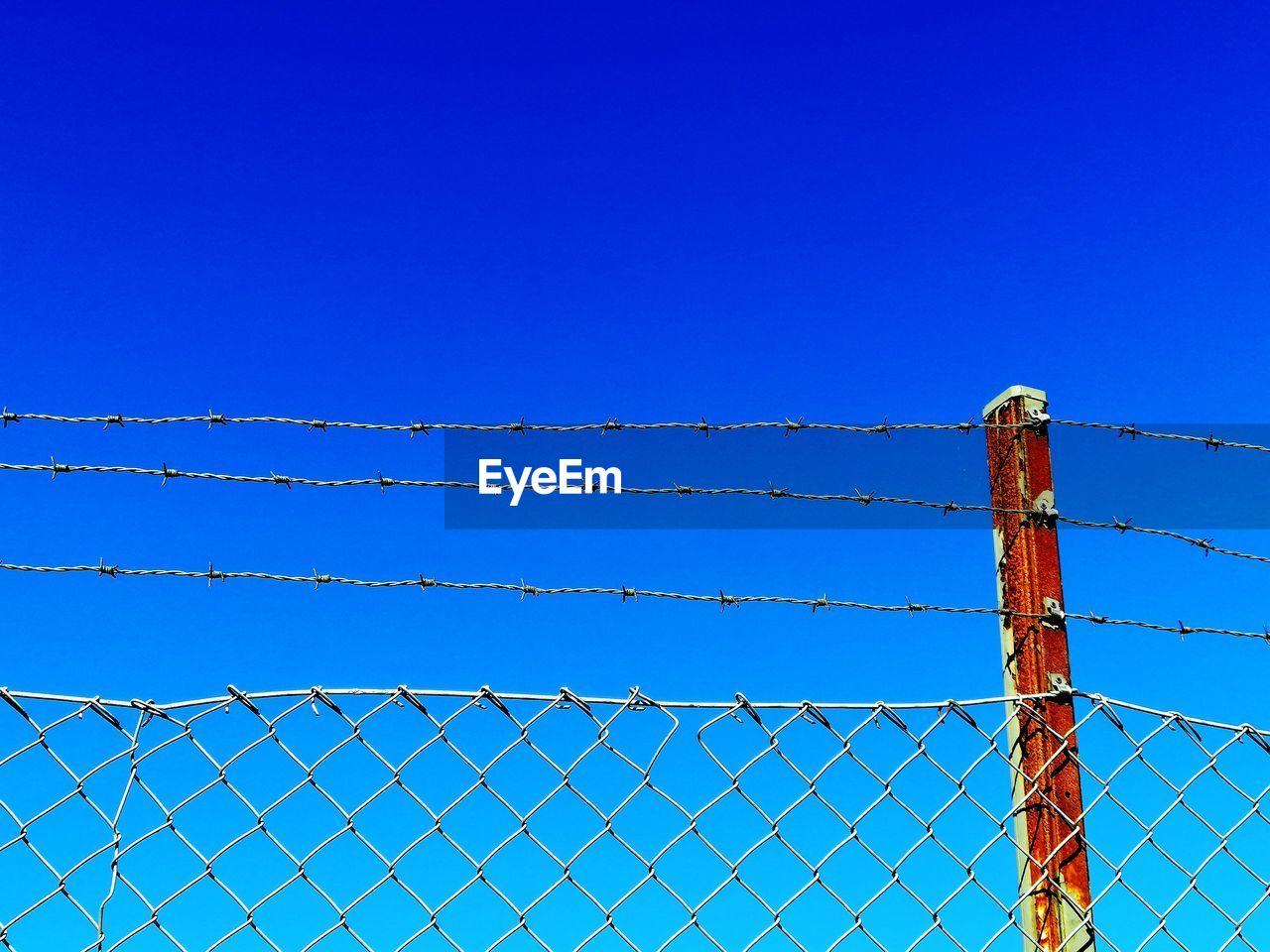 Low angle view of fence against blue sky