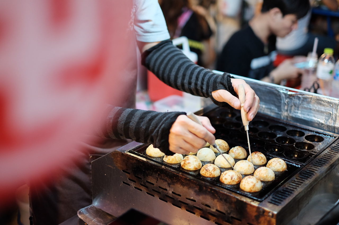 Cropped image of person cooking takoyaki at food market