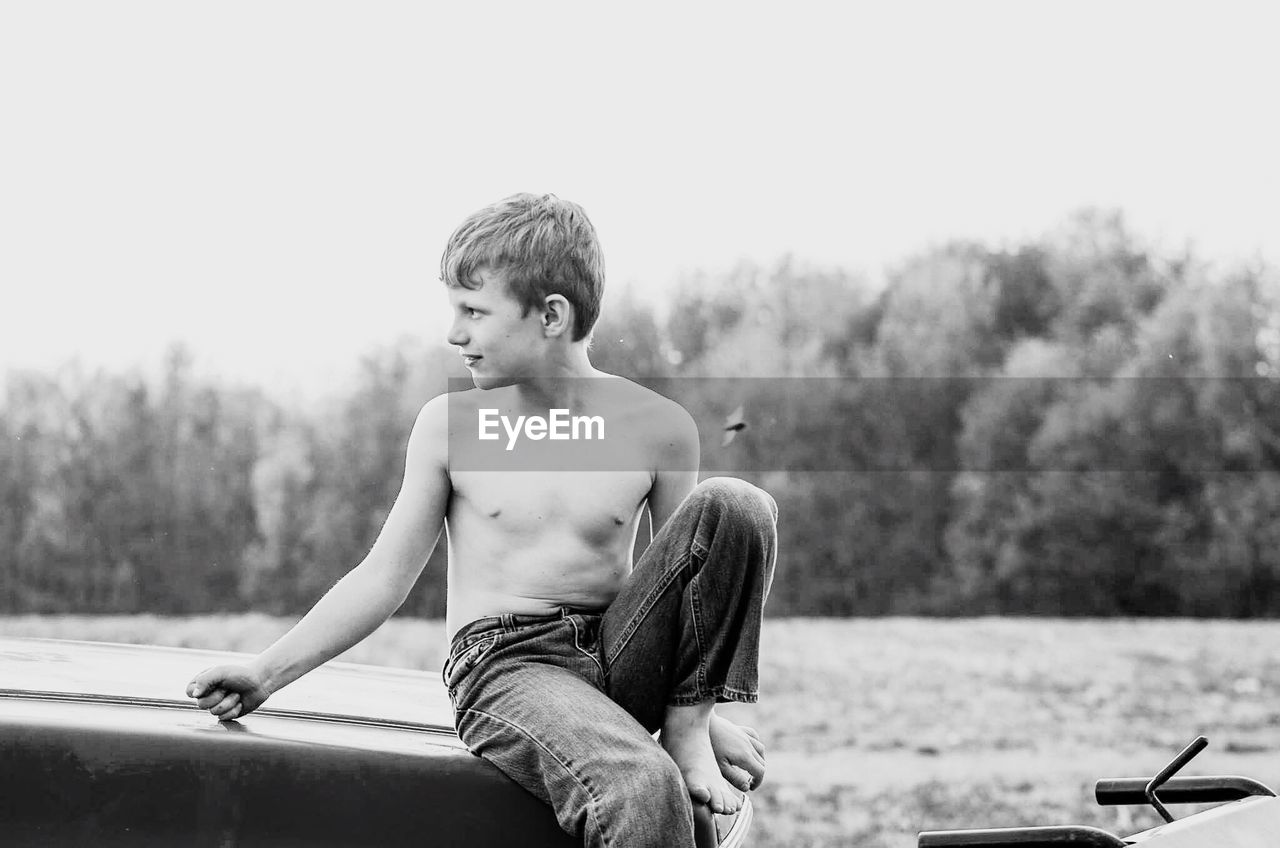 Full length of shirtless boy sitting against sky