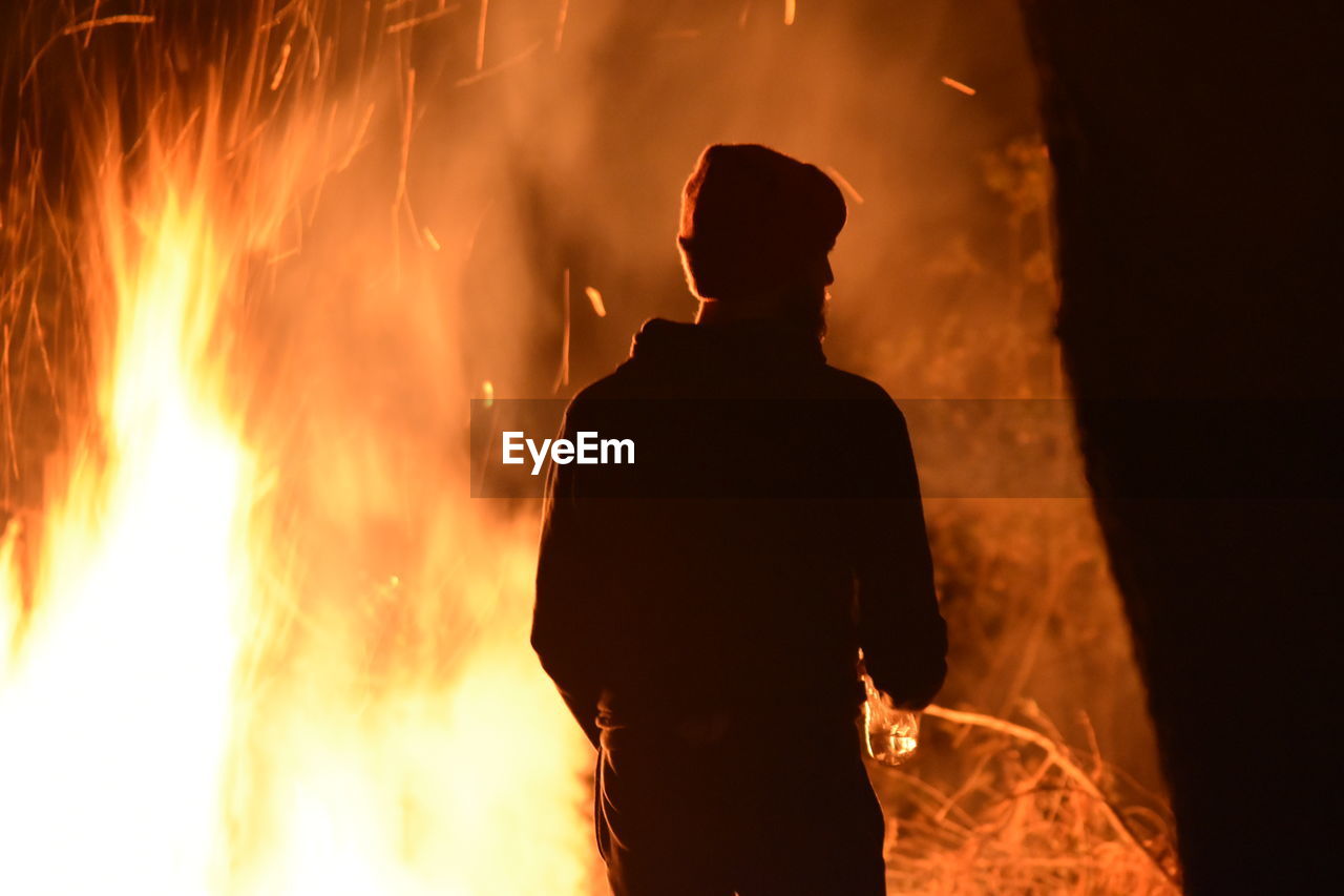 Rear view of silhouette man against fire at night