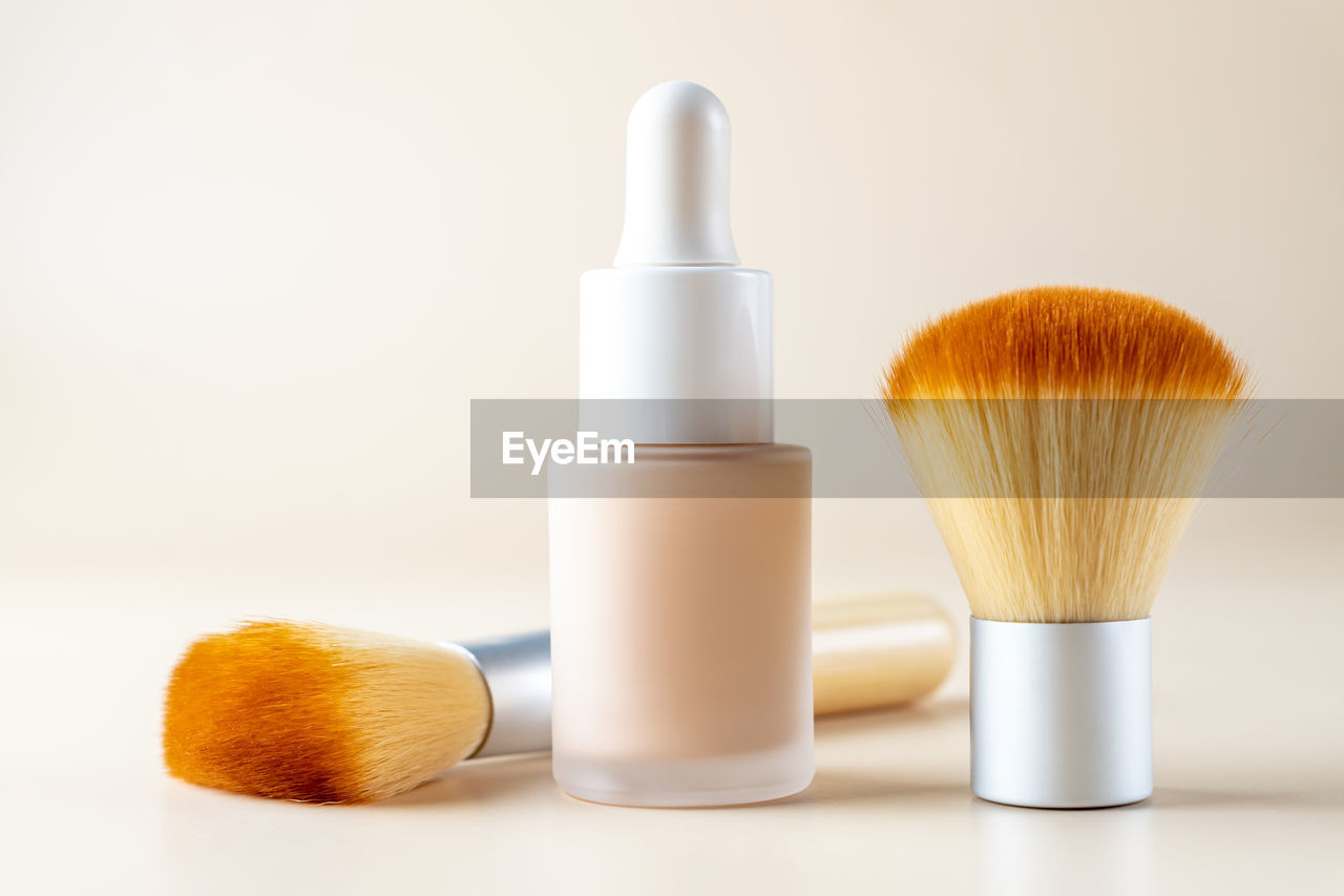 Liquid foundation in a bottle and a cosmetic brushes. facial corrector on beige background