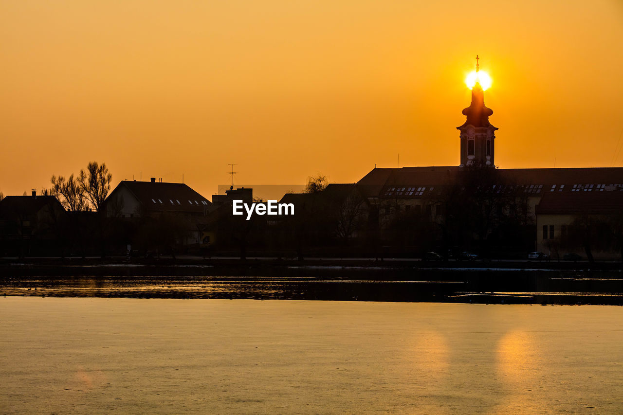 Illuminated city at waterfront during sunset