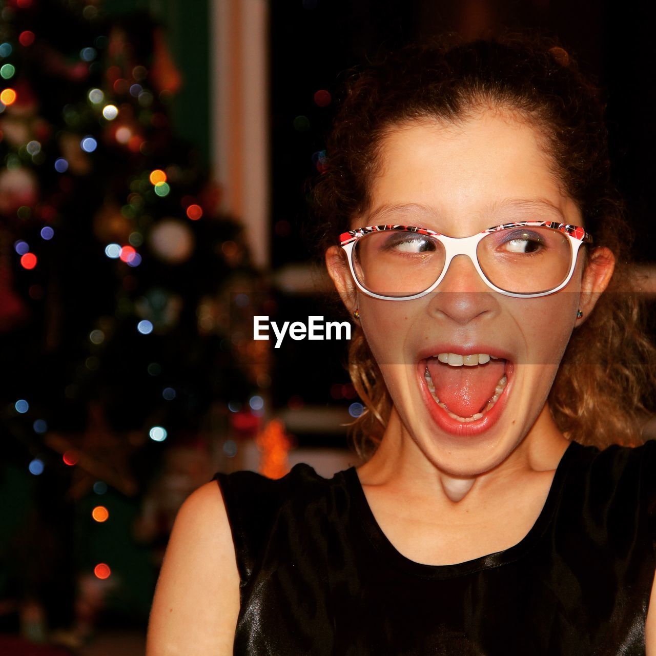 Excited woman with mouth open sideways glancing against christmas tree