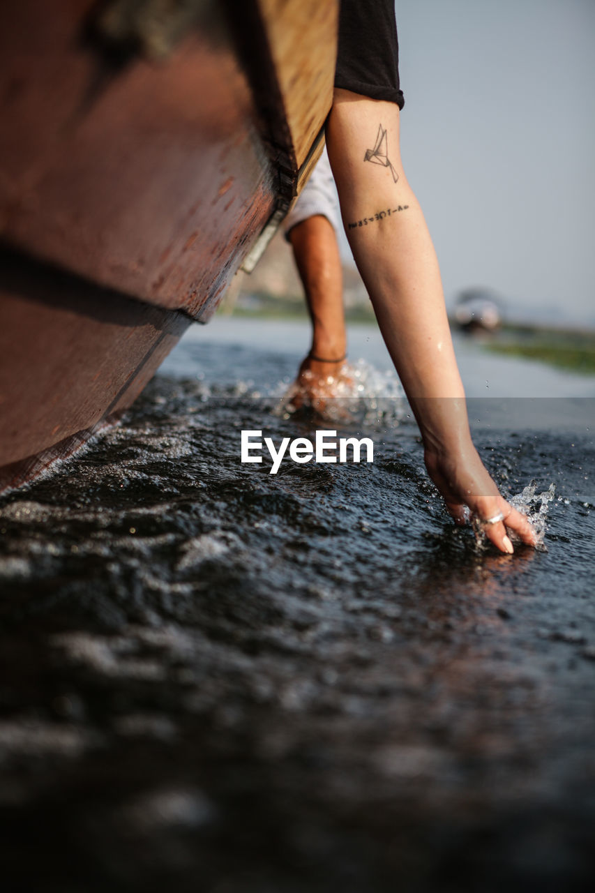 Cropped image of hands touching water while traveling in boat