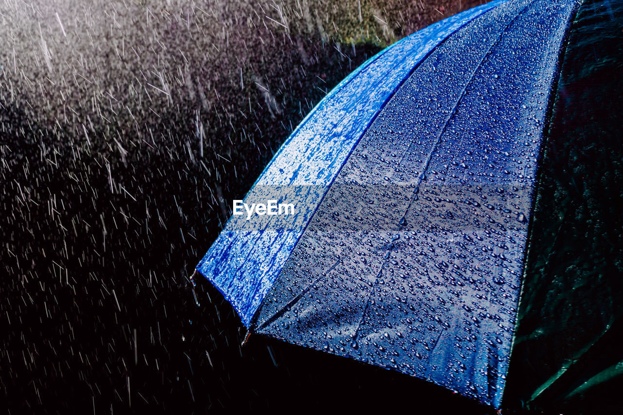 Raindrops splashing on blue umbrella during monsoon