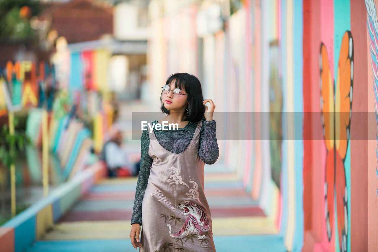 YOUNG WOMAN LOOKING DOWN WHILE STANDING AGAINST WALL