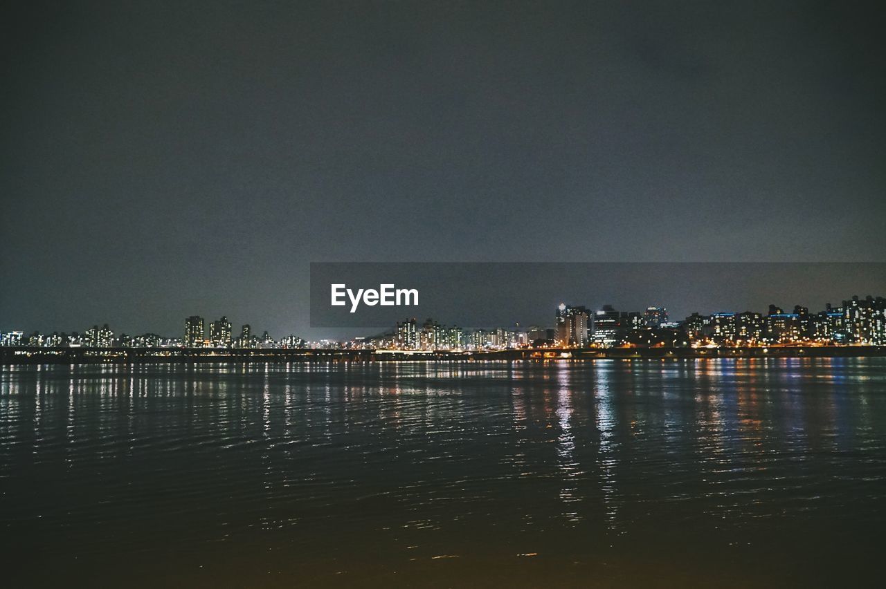 Illuminated cityscape by sea against sky at night