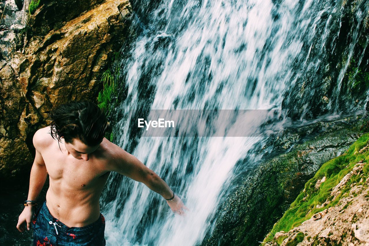 High angle view of shirtless man standing at waterfall