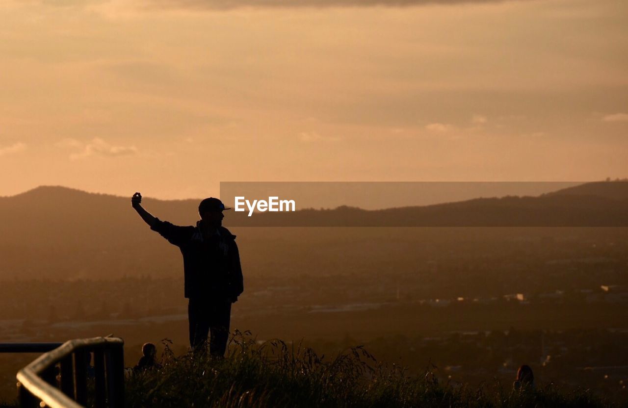 REAR VIEW OF SILHOUETTE MAN STANDING AGAINST SKY DURING SUNSET