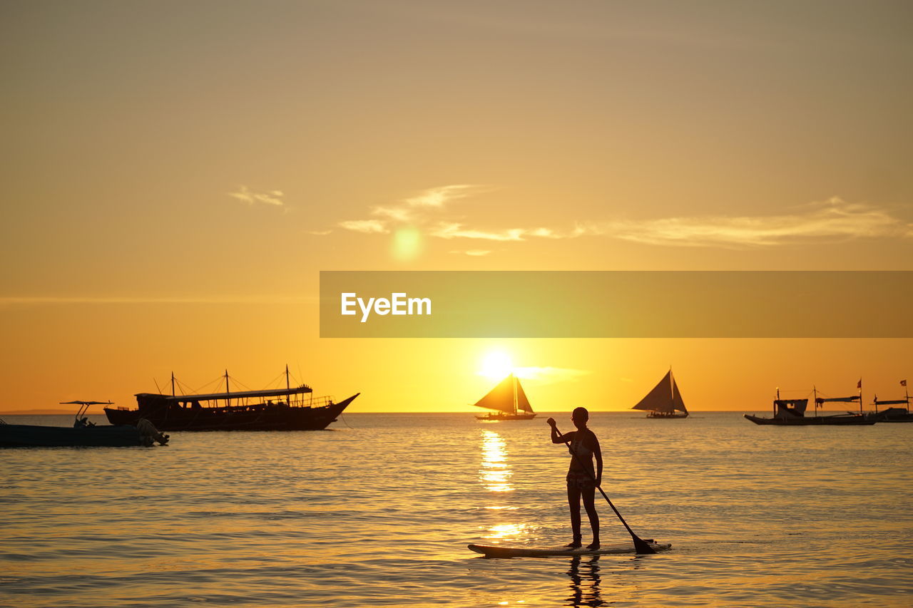 Silhouette woman paddleboarding in sea against sky during sunset