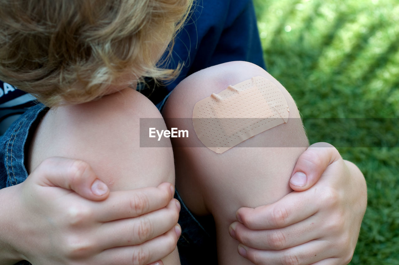 High angle view of boy with adhesive bandage on knee sitting on grass