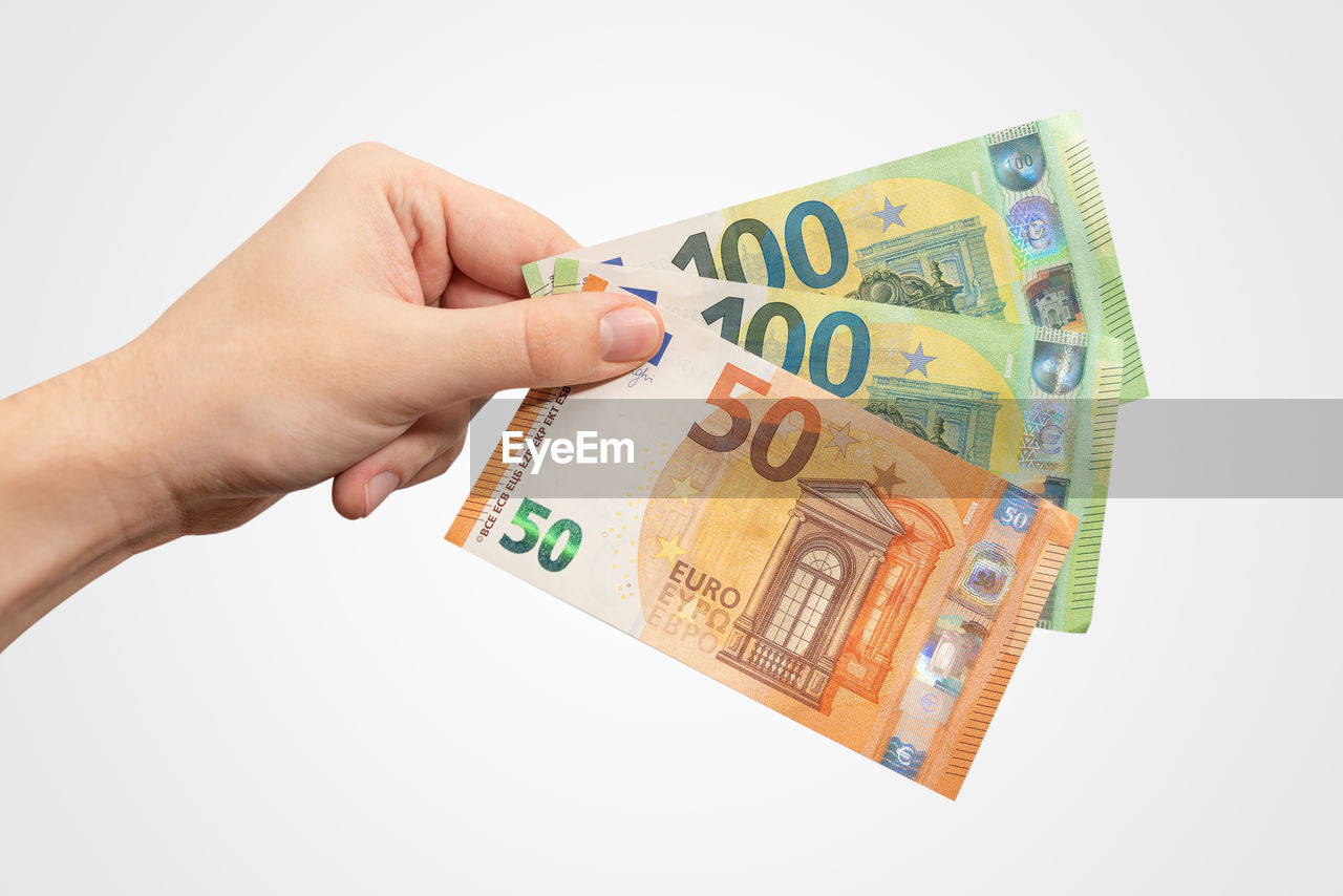 Close-up of hand holding paper currency against white background