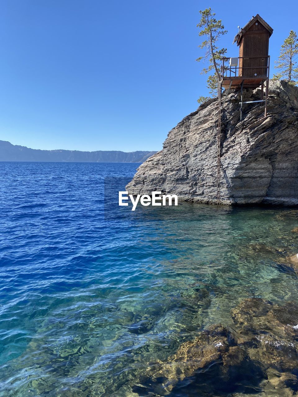 blue, water, nature, cliff, terrain, day, sky, no people, sea, architecture, outdoors, reflection, built structure, clear sky, rock, beauty in nature, scenics - nature, low angle view, tree