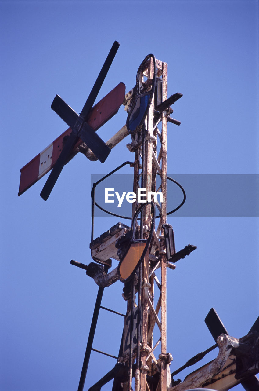 Low angle view of old railroad crossing sign against clear blue sky