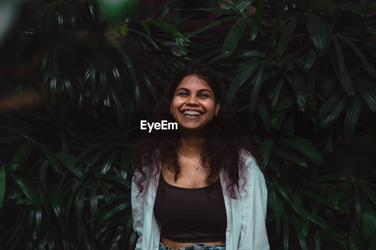 Portrait of young woman standing against plants