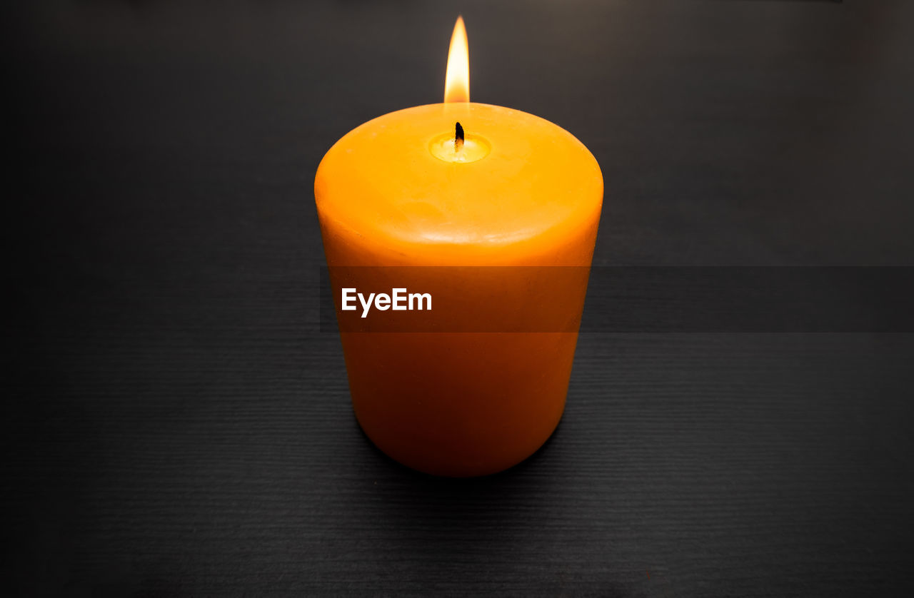 CLOSE-UP OF ORANGE CANDLE ON TABLE WITH LIGHT