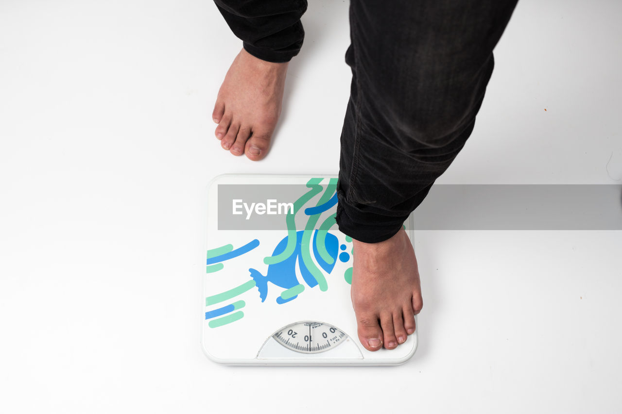 Low section of man standing over weight scale against white background