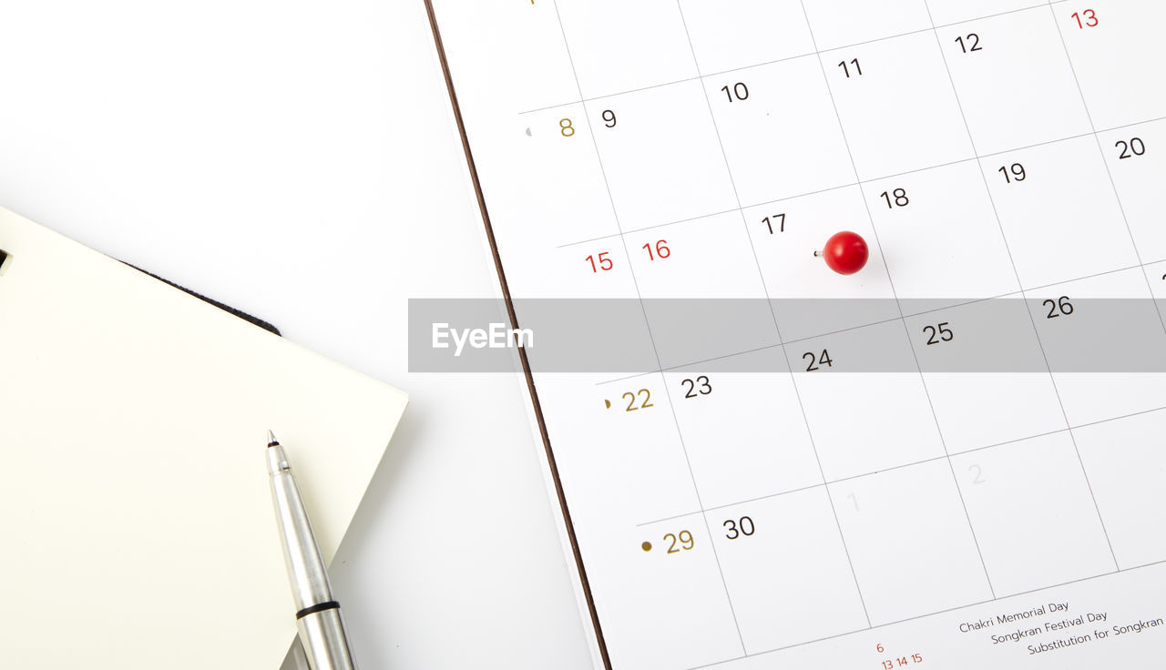 Close-up of diary with pen and thumbtack pinned calendar on table