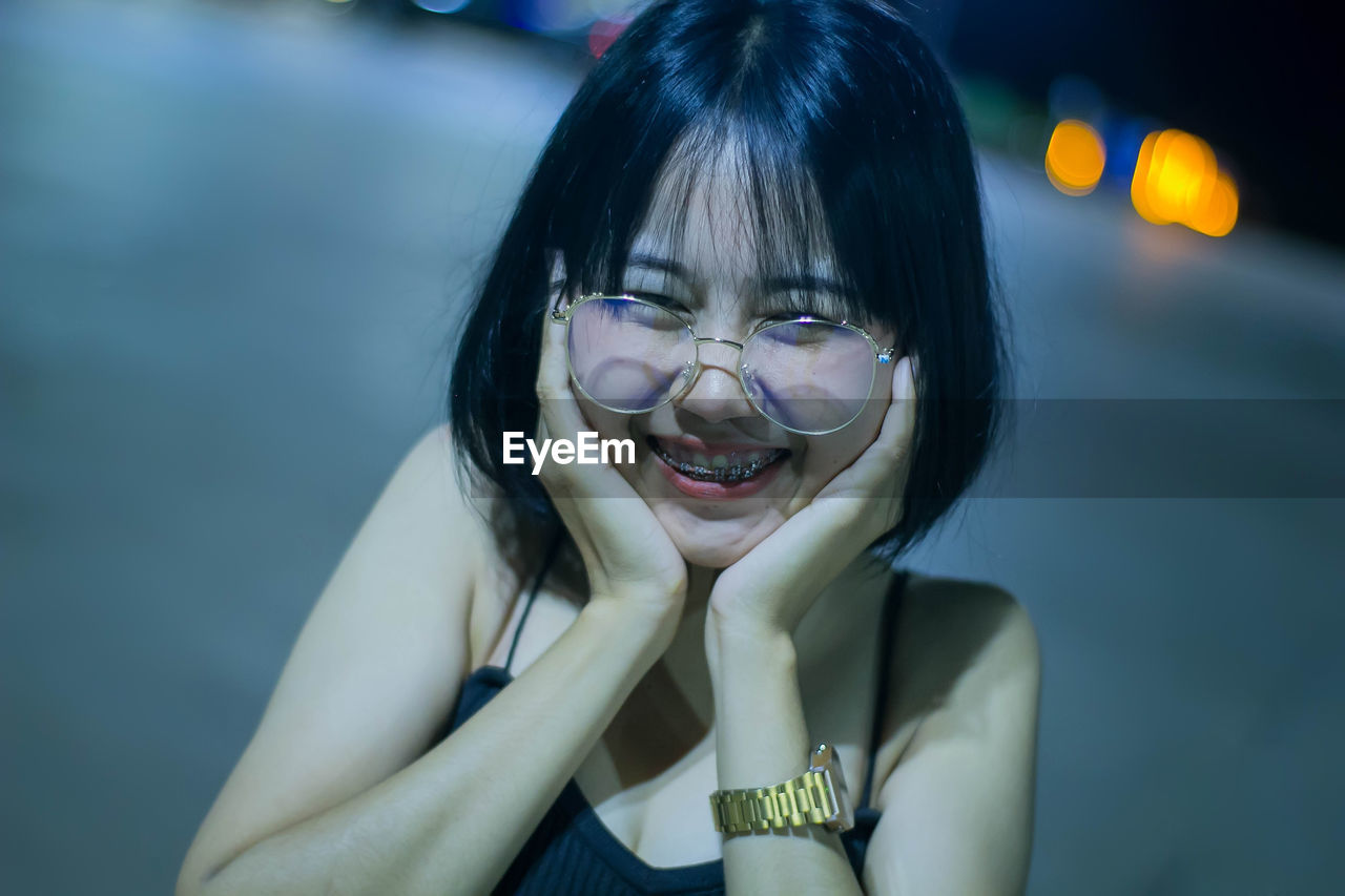 Portrait of smiling woman with hands on chin standing outdoors at night