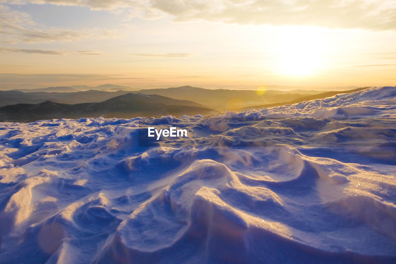 AERIAL VIEW OF SNOWCAPPED MOUNTAINS AGAINST SKY AT SUNSET