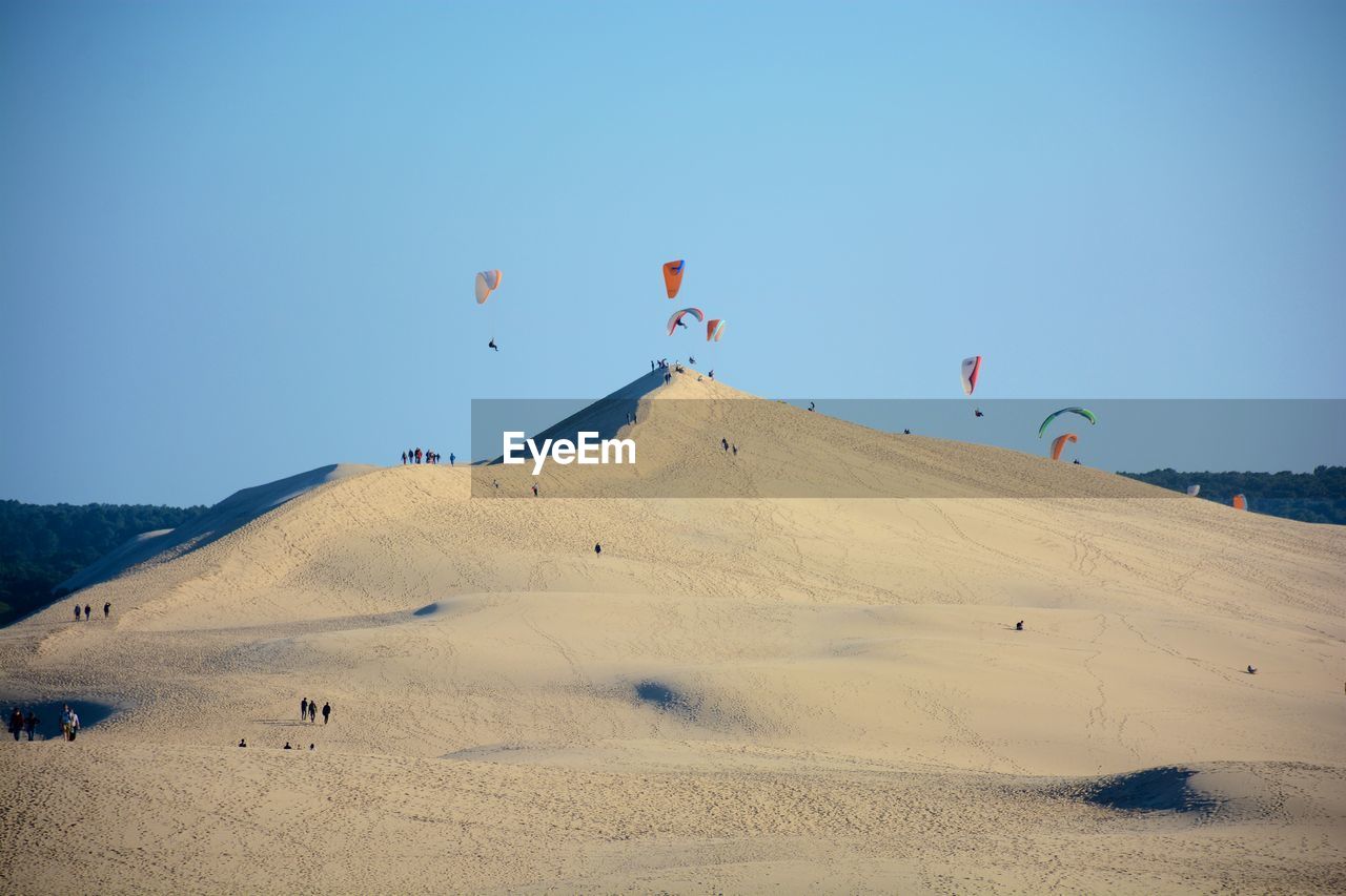 Kites flying over dune of pilat against clear sky