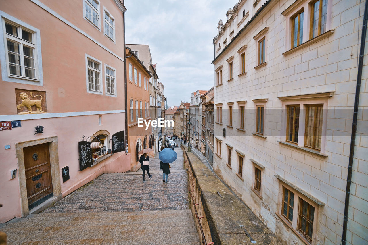 REAR VIEW OF MEN WALKING ON STREET AMIDST BUILDINGS