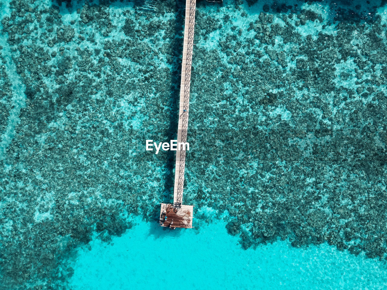 Top down aerial view over the end of wooden jetty with unidentified kids on it.