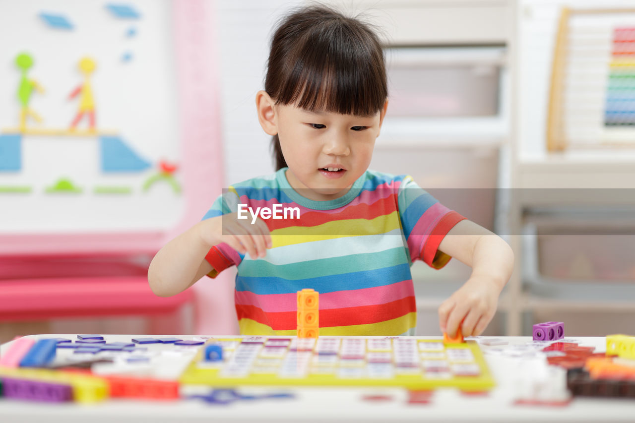 Cute girl playing with building blocks at classroom